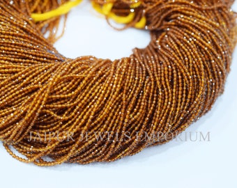 May include: A close-up of a strand of brown faceted gemstone beads. The beads are small and round, and they are strung together on a clear thread. The beads are arranged in a circular pattern, and they are all facing the same direction. The beads are shiny and reflect light.
