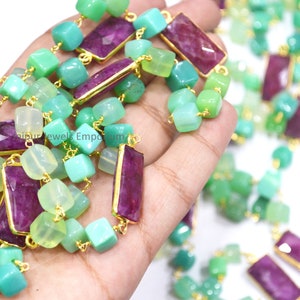 May include: A strand of beads with a gold chain. The beads are green, light green, and purple. The chain is gold and has a square shape.