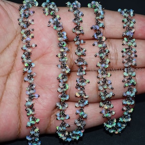 May include: A strand of black metal chain with small, iridescent opal beads. The chain is made of small, linked metal rings with a cluster of opal beads hanging from each ring.