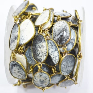 May include: A close-up of a chain made of oval-shaped, gray and white agate stones with brass accents. The chain is wrapped around a spool.