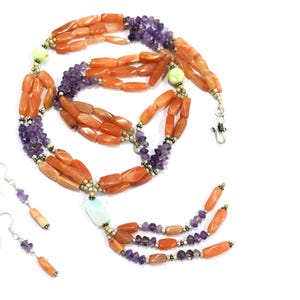 May include: A multi-strand necklace and matching drop earrings set featuring orange cylindrical beads, purple amethyst chip beads, small metallic spacer beads, and a single light green accent bead, finished with a silver-toned hook clasp.