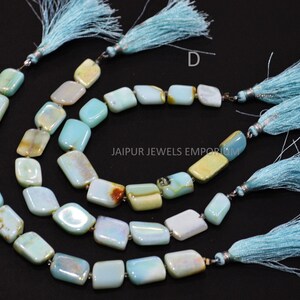 May include: Gemstone bead strands in pale blue, yellow, and brown hues. Each strand is finished with a light blue tassel. The rectangular beads are strung together. The text "JAIPUR JEWELS EMPORIUM" is visible.