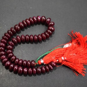 Peut inclure: Un chapelet de perles polies rouge foncé, accompagné d'un pompon rouge vif. Les perles sont de taille uniforme et enfilées ensemble. Le pompon est fait de fils fins et fluides.
