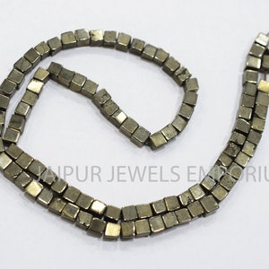 Puede incluir: Una hebra de cuentas de pirita, cada cuenta tiene forma de cubo, las cuentas son de color gris oscuro con un brillo metálico.