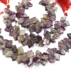 May include: Strands of faceted gemstone beads in shades of purple, grey, and clear. The beads are strung together, with red tassels at the ends. The gemstones have a geometric shape.