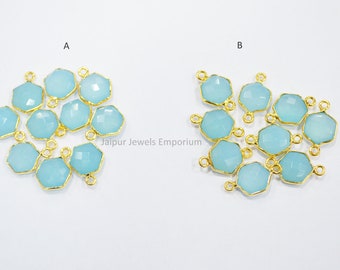 Puede incluir: Dos grupos de dijes de piedra preciosa azul claro con detalles de metal dorado. Cada dije tiene dos anillos de salto para sujetarlo a joyas. Los dijes están dispuestos en un grupo suelto. El texto "Jaipur Jewels Emporium" es visible en el centro de la imagen.