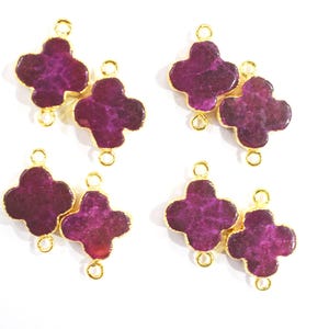 Può includere: Sei connettori per gioielli a forma di trifoglio in metallo dorato con un intarsio in pietra viola scuro e strutturata. Ogni connettore ha due forme di trifoglio collegate da piccoli anelli dorati, perfetti per la creazione di gioielli.