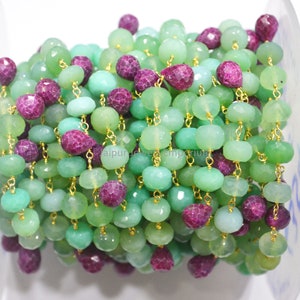Op de afbeelding: Een kralenketting met afwisselende groene en paarse edelstenen. De groene kralen zijn in verschillende vormen en maten, terwijl de paarse kralen facetgeslepen zijn. De kralen zijn geregen met goudkleurig draad, waardoor een decoratief sieradenonderdeel ontstaat.