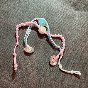 May include: A pink and white beaded bracelet with blue and white beads and two silver buttons.