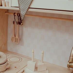 May include: A wooden play kitchen set with a white sink, a stovetop, and a wooden countertop. There are two wooden candlesticks with white candles on the countertop. The countertop has a sign that says "Pretty Little Kitchen".