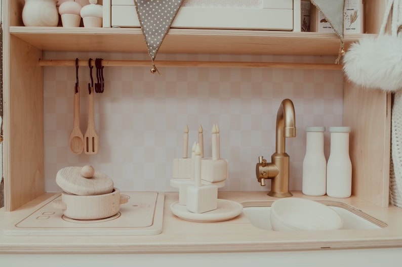 May include: A wooden toy kitchen playset with a gold faucet, a wooden pot with a lid, a wooden cake with candles, and two wooden milk bottles.