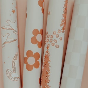 May include: Four rolls of white wrapping paper with different patterns in orange. The patterns include a flower, a Christmas tree, a dove with stars, and a checkered pattern.