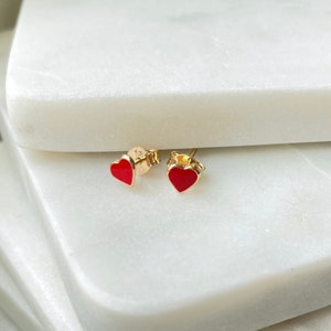 May include: A pair of gold heart-shaped earrings with red enamel.