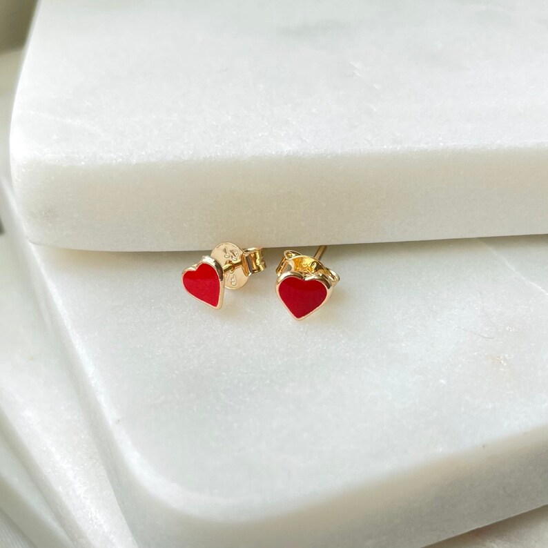 May include: A pair of gold heart-shaped earrings with red enamel.
