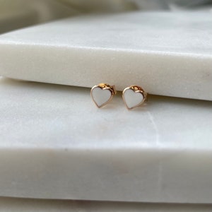 May include: A pair of gold heart-shaped earrings with white enamel centers.