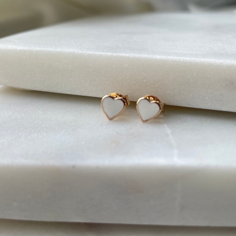 May include: A pair of gold heart-shaped earrings with white enamel centers.
