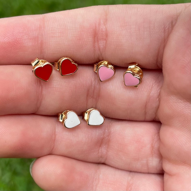 May include: A set of six heart-shaped stud earrings in red, pink, and white. The earrings are made of gold-toned metal and have a small heart-shaped charm in the center.