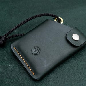 May include: A black leather wallet with a gold snap closure and a brown stitching detail. The wallet has a small logo that says "Unknown Goods Co."