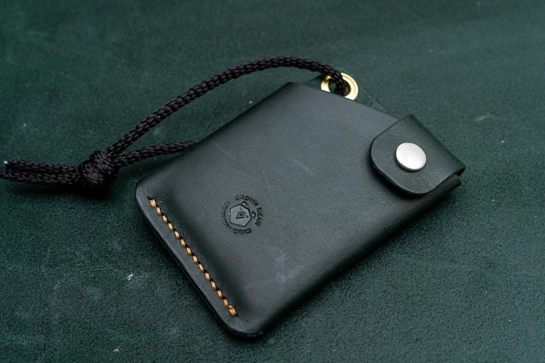 May include: A black leather wallet with a gold snap closure and a brown stitching detail. The wallet has a small logo that says "Unknown Goods Co."
