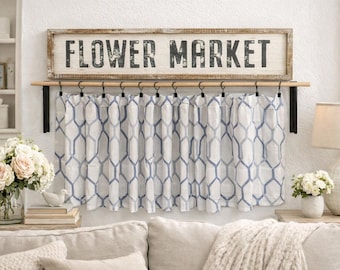 May include: A decorative wooden sign with the text "FLOWER MARKET" hangs above a curtain with a blue and white geometric pattern. The scene includes a sofa, flowers, and a lamp.