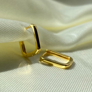 Könnte beinhalten: Ein Paar goldene quadratische Creolen. Die Ohrringe sind schlicht und elegant und würden eine großartige Ergänzung für jede Schmucksammlung sein.