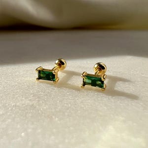 Può includere: Un paio di orecchini a perno dorati con pietre rettangolari verde smeraldo.