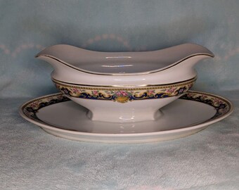 May include: A white porcelain gravy boat and matching underplate. The boat has a curved handle and a decorative band with floral and gold accents. The underplate has a matching border design. A classic serving set.