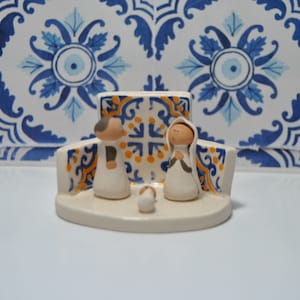 May include: A ceramic nativity scene with a blue and white tiled background. The figures are white with brown accents and depict Mary, Joseph, and the baby Jesus.