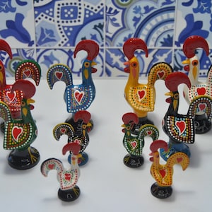Pode incluir: Uma coleção de estatuetas de galo coloridas, cada uma pintada com detalhes intrincados e com um design de coração vermelho. Os galos são de cerâmica e vêm em vários tamanhos.