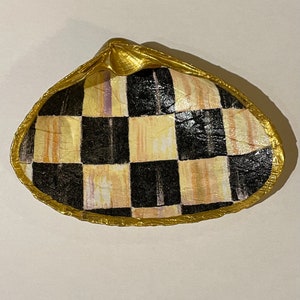May include: Clam shell with a gold rim and a black and cream chequered pattern inside. The shell is set against a white background. The design highlights the contrast between the gold, black, and cream colours.