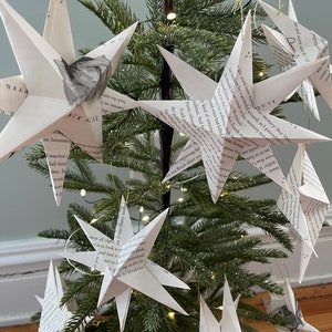 May include: A Christmas tree decorated with white paper stars made from book pages. The stars are hanging from the tree branches with gold string. The tree is decorated with white lights. The text on the stars is from the Harry Potter books.