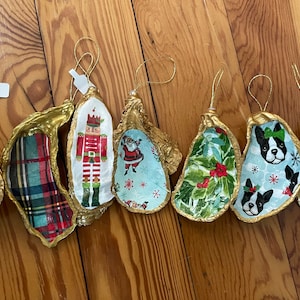 Peut inclure: Huit ornements en forme d'huître avec une bordure dorée et différents motifs sur le thème des fêtes, notamment un casse-noisette, le Père Noël, du tartan et un chien.