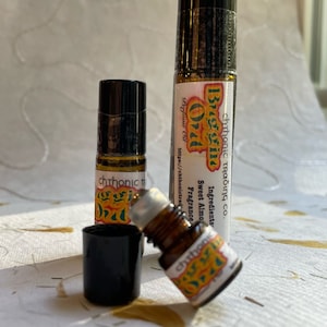 May include: Three glass bottles with black caps and labels that say "Bugging Oil" and "chthonic Trading Co.". The labels are yellow, green, and orange. The bottles are filled with a clear liquid.