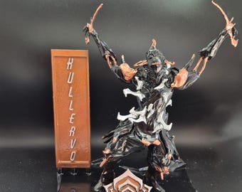 May include: A black and silver 3D printed figurine of a character from the video game Warframe. The figurine is posed with arms raised and is standing on a black base with a copper-colored symbol. The figurine is labeled "HULLER VO" on a copper-colored plaque.