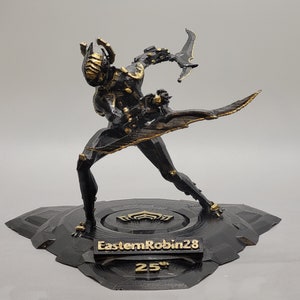 May include: A black and gold figurine of a character in a dynamic pose, holding a blade. The figurine is on a black base with the text "EasternRobin28" and "25th". The figure has a detailed design.