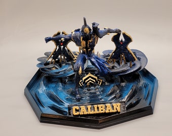 May include: A blue and gold 3D printed figurine of a character from the video game Warframe. The character is named "Caliban" and is standing on a blue and black base.