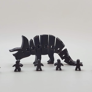 May include: A black articulated triceratops dinosaur toy with seven smaller black figures standing in front of it.