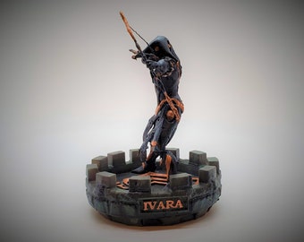 May include: A black and gold 3D printed figurine of a hooded figure holding a bow and arrow. The figure is standing on a green and brown base with the word "IVARA" inscribed on it.