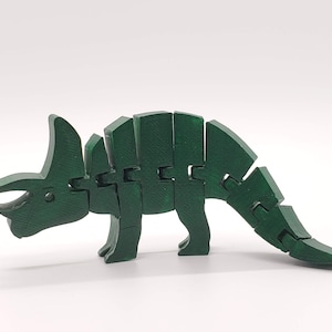 May include: A green articulated toy dinosaur, resembling a Triceratops, with a large frill and three horns. The toy is made of plastic and is designed to be flexible and bendable.