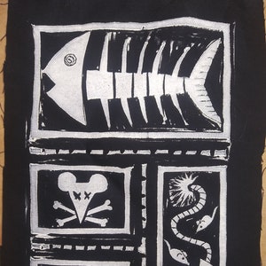 Pode incluir: Ilustração em preto e branco de um esqueleto de peixe, um rato com uma caveira e ossos cruzados, um rato com uma bola de lã e o texto "PAWS OFF!" sobre um fundo preto.