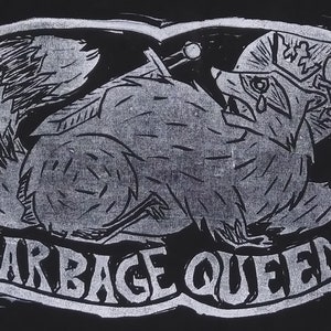 Op de afbeelding: Zwart-witte illustratie van een wasbeer die een kroon draagt en een stok vasthoudt. De tekst "GARBAGE QUEEN" staat onder de wasbeer.