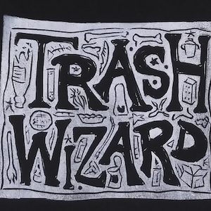 Puede incluir: Un estampado gráfico en blanco y negro con el texto TRASH WIZARD en letras negritas dibujadas a mano. El diseño está rodeado de pequeñas ilustraciones esquemáticas de varios objetos desechados, incluyendo botellas, huesos, cajas y utensilios.