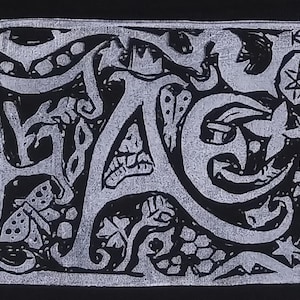 以下が含まれることがあります： 文字の周りに複雑なデザインとパターンが施された、白黒のグラフィックプリントの「HAG」という単語です。