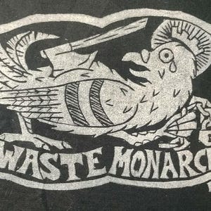 Op de afbeelding: Zwart-wit grafisch ontwerp met een vogelachtig wezen met een zwaard, een kroon en een traan. De tekst "WASTE MONARCH" wordt onder het wezen weergegeven in een decoratieve rand. Het ontwerp heeft een vintage, handgetekende uitstraling.