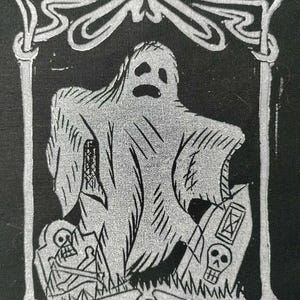 May include: A black and white illustration of a ghost with a sad expression, standing in front of two tombstones with skulls. The ghost is inside a decorative frame. The image has a Halloween theme.