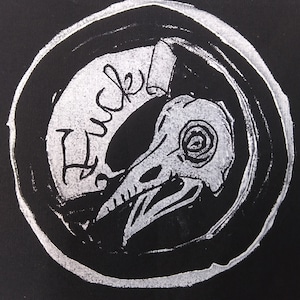 Op de afbeelding: Een zwart-wit cirkelvormig ontwerp met een schedel van een vogel en het woord "Huck" in cursief.