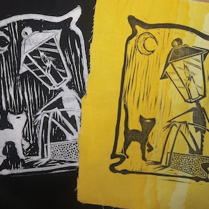 May include: Two black and white linocut prints on fabric. The prints depict a cat walking past a street lamp with a crescent moon in the background. One print is on a black background and the other is on a yellow background.