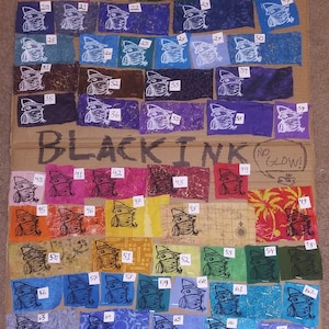 May include: A cardboard sample board with fabric swatches showing different colors of white and black ink. The swatches are numbered 1 through 87. The text "WHITE INK" and "BLACK INK" are written at the top of the board. The text "CAN BE GLOW IN THE DARK!" is written next to the white ink swatches. The text "NO GLOW!" is written next to the black ink swatches.