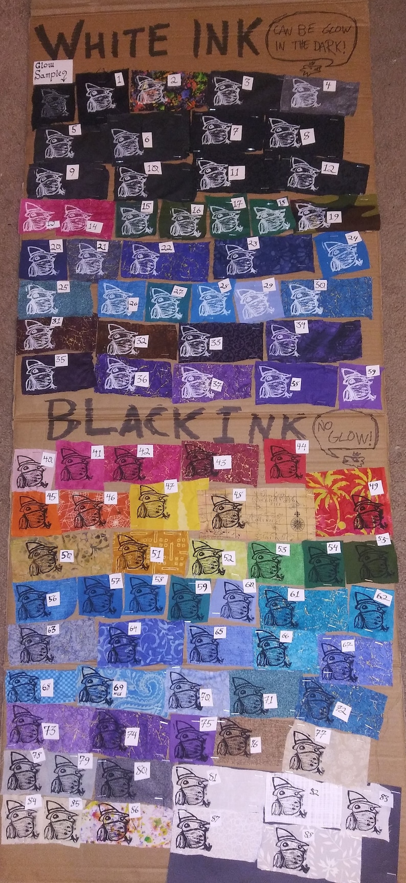 May include: A cardboard sample board with fabric swatches showing different colors of white and black ink. The swatches are numbered 1 through 87. The text "WHITE INK" and "BLACK INK" are written at the top of the board. The text "CAN BE GLOW IN THE DARK!" is written next to the white ink swatches. The text "NO GLOW!" is written next to the black ink swatches.