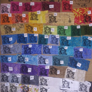 May include: A collection of 88 fabric squares with a black ink stamp of a frog wearing a hat. The fabric squares are arranged in rows and columns on a brown cardboard background. The fabric squares are in various colors and patterns. The text "BLACK INK NO GLOW!" is written at the top of the image.